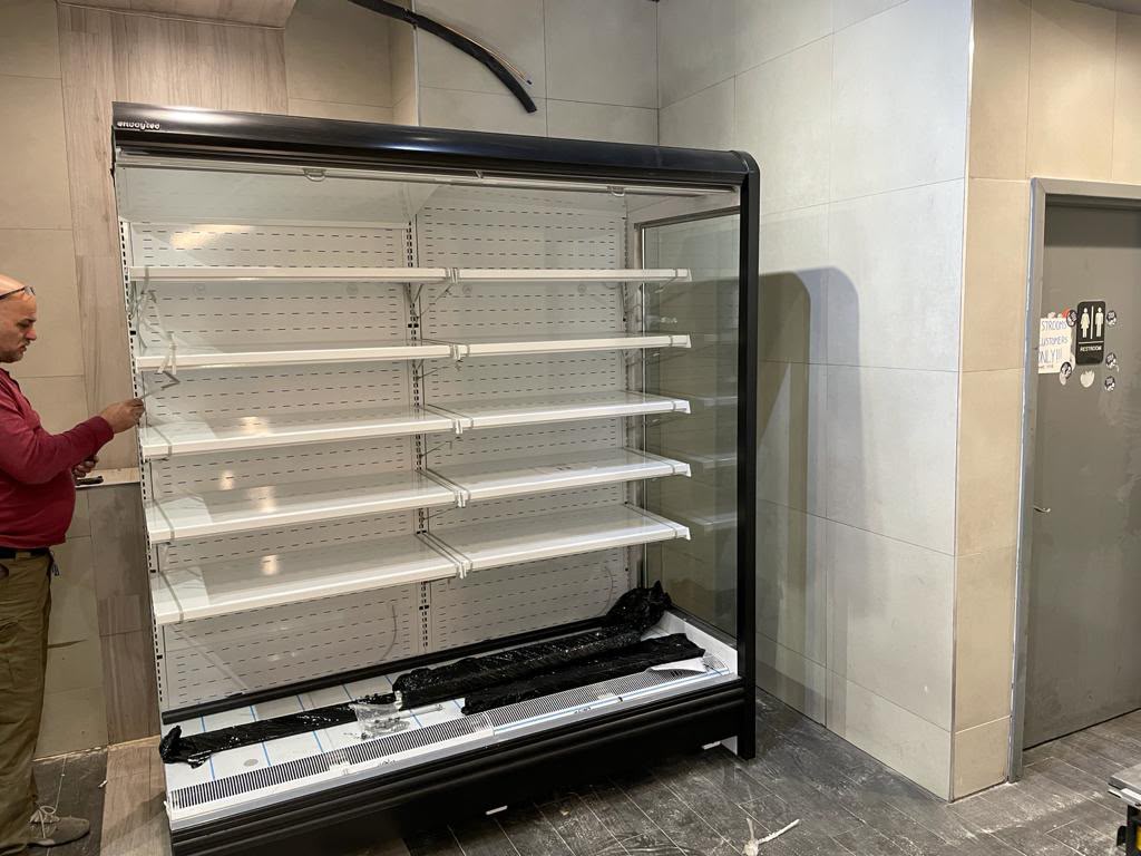 Open-air refrigerated merchandiser being set and leveled by a technician