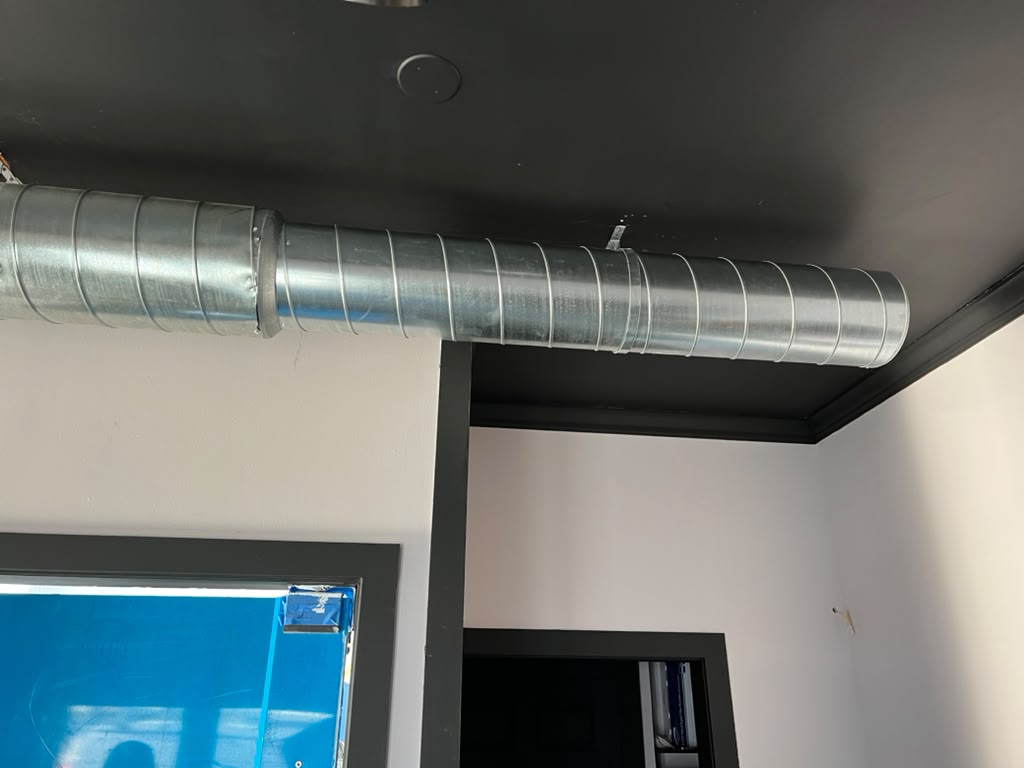 Round spiral duct run installed along an exposed black ceiling